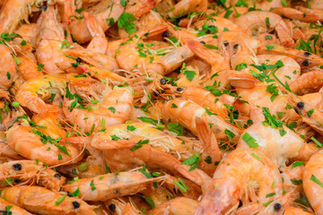 Close up of large portion of cooked shrimps with tomato sauce and green parsley in a large pan at a street food festival, ready to eat healthy seafood, beautiful orange monochrome outdoor background.