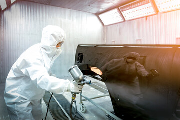 automobile repairman painter in protective workwear and respirator painting car body in paint...