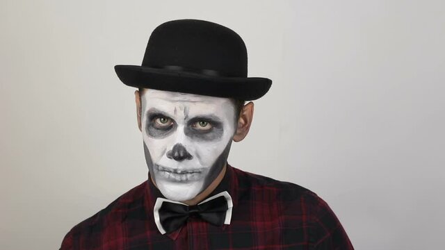 A hideous man in clown makeup raises his hat to greet his victim. The scary clown looks at the camera and laughs terribly and threatens his victim. Scary grimaces of a clown looking at the camera.  