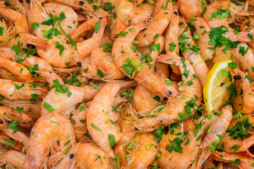 Close up of large portion of cooked shrimps with tomato sauce and green parsley in a large pan at a street food festival, ready to eat healthy seafood, beautiful orange monochrome outdoor background.