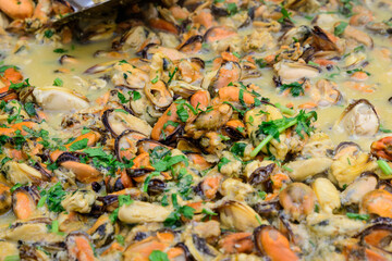 Large group of cooked mussels with tomato and cream sauce at a street food festival, ready to eat seafood,  beautiful orange monochrome outdoor background.