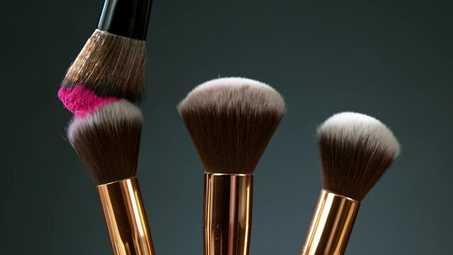 Makeup brushes touch each other on dark background and small particles of cosmetics, super slow motion, 1000 fps.