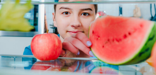 Teenage  Girl standing near open fridge full of healthy food, vegetables and fruits. Looking Inside Fridge