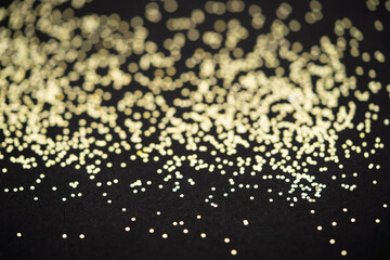 Beautiful Christmas light background. Abstract glitter bokeh and scattered sparkles in gold, on black