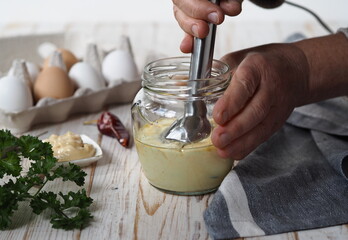 The concept of making homemade mayonnaise from natural healthy ingredients.An elderly woman prepares homemade mayonnaise in a jar with vegetable oil and an egg