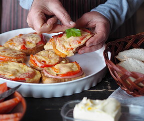 An elderly woman cooks hot sandwiches for the family with cheese, tomatoes, sausage on toast.Healthy natural food.