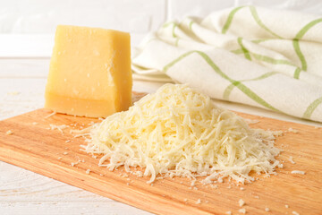 Heap of grated italian hard cheese Grana Padano or Parmesan on a wood cutting board over white wood table. Delicious ingredient for pizza, sandwiches, salads.