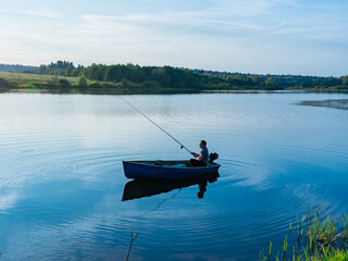 Elderly man fishing with a rod on a small fishing boat on the lake 