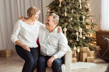 Senior couple smiling beside their christmas tree at home in the living room