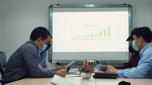 Businessmen wearing protective masks discussing and work together in meeting room. Social distance practice prevent coronavirus COVID-19.