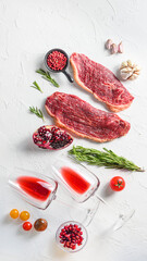 Picanha beef  steak with glasses of red wine ,  rosemary and pomegranate top view over white textured background . Big size.