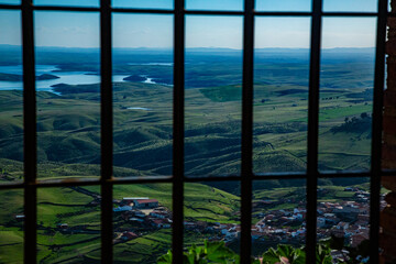 Paisaje de valle y montañas con embalse desde ventana con rejas