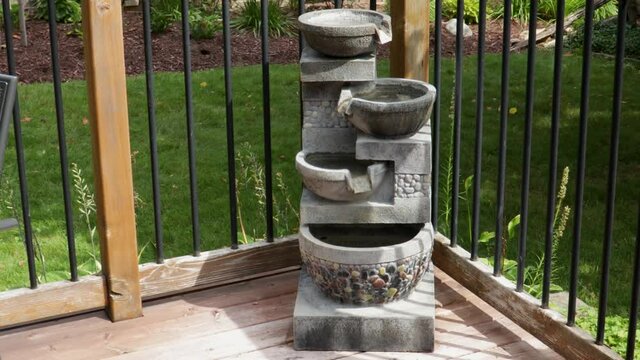 At the corner of a wooden deck, water starts pouring from the top basin  of a fountain into subsequent levels from a recirculating pump.