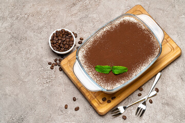 Traditional Italian Tiramisu dessert in glass baking dish on concrete background