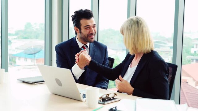 Two happy business people celebrate at office meeting room. Successful businessman congratulate project success with colleague at modern workplace while having conversation on financial data report.
