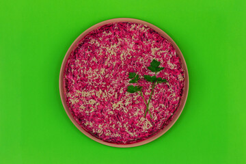 traditional Russian holiday salad Herring under a fur coat (shuba) with sprigs of fresh green parsley on a green background top view