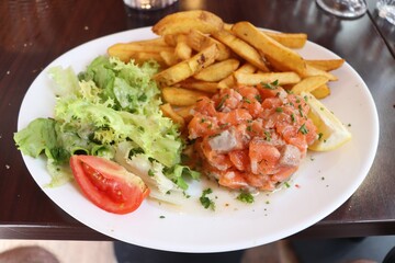 Tartare de saumon accompagné de frites et de salade dans une assiette blanche, saumon cru assaisonné, ville de Lyon, département du Rhône, France