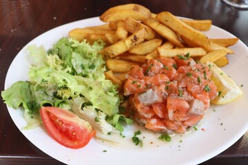 Tartare de saumon accompagné de frites et de salade dans une assiette blanche, saumon cru assaisonné, ville de Lyon, département du Rhône, France