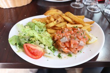 Tartare de saumon accompagné de frites et de salade dans une assiette blanche, saumon cru assaisonné, ville de Lyon, département du Rhône, France