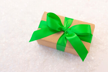 Gift wrapped in craft paper and decorated with green ribbon flat lay with snow on background.