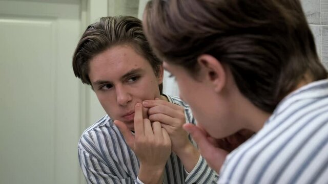 Young guy crushes pimples in bathroom. Awkward age. Problems skin. Dermatology
