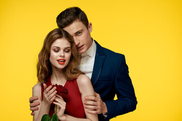 A romantic man hugs a woman in a red dress with a rose in his hand on a yellow background