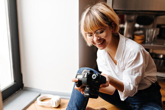 Joyful girl holding camera with smile. Pleased female photographer in glasses expressing happiness.