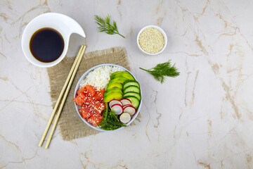 Poke bowl with salmon, rice, avocado, radish, cucumber, sesame seeds and seaweeds.  Asian trendy, diet food. Top view. Flat lay.