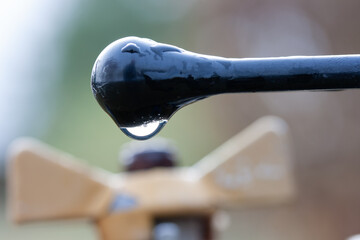 A drop of water on a black handle on the background of a yellow tap