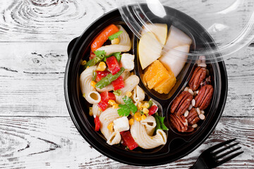 Lunch box set. Pasta salad, slices of fruit and mix of nuts in the disposable bowl on the white table