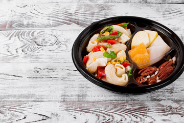 Lunch box set. Pasta salad, slices of fruit and mix of nuts in the disposable bowl on the white table