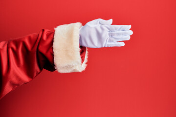 Hand of a man wearing santa claus costume and gloves over red background stretching and reaching with open hand for handshake, showing palm