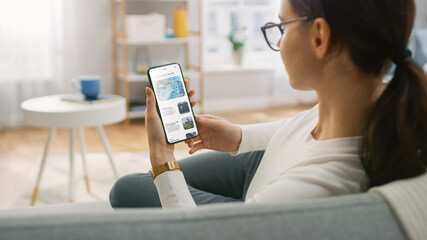 Young Woman at Home Uses Smartphone for Scrolling and Reading News about Technological...
