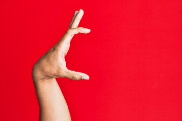 Arm of caucasian white young man over red isolated background picking and taking invisible thing, holding object with fingers showing space