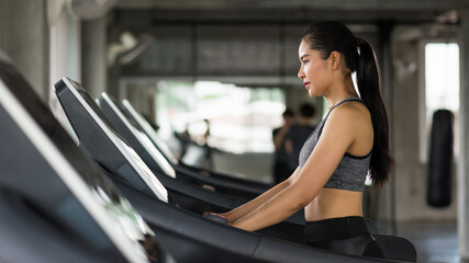 Fototapeta na wymiar Asian attractive sporty woman walk cardio training on treadmills to warm up before running in fitness gym with copy space for text. Bodybuilding and healthy lifestyle concept.