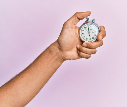 Hand of young hispanic man using stopwatch over isolated pink background.