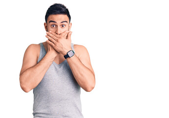 Young handsome man wearing swimwear and sleeveless t-shirt shocked covering mouth with hands for...