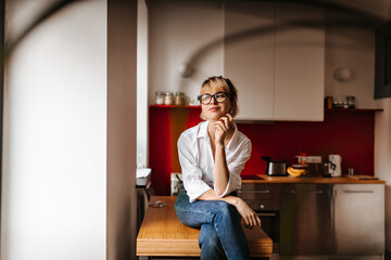 Selective focus of trendy girl sitting on table. Dreamy european lady posing at home in morning.