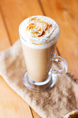 Pumpkin latte on a wooden background. Pumpkin spice latte with whipped cream on a burlap. Minimalism