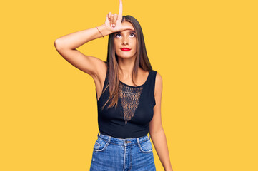 Young hispanic woman wearing casual clothes making fun of people with fingers on forehead doing loser gesture mocking and insulting.