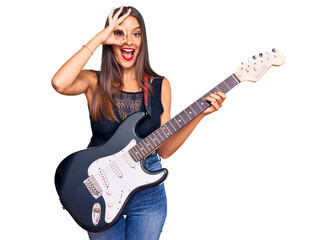 Fototapeta premium Young hispanic woman playing electric guitar smiling happy doing ok sign with hand on eye looking through fingers