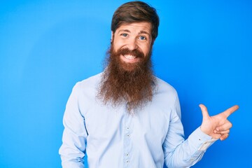 Handsome young red head man with long beard wearing elegant clothes smiling cheerful pointing with hand and finger up to the side