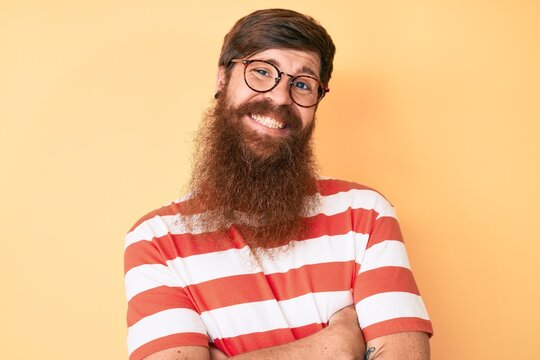 Handsome young red head man with long beard wearing casual clothes and glasses happy face smiling with crossed arms looking at the camera. positive person.