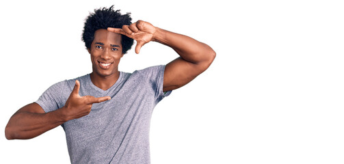 Handsome african american man with afro hair wearing casual clothes smiling making frame with hands and fingers with happy face. creativity and photography concept.