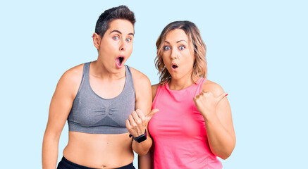 Couple of women wearing sportswear surprised pointing with hand finger to the side, open mouth amazed expression.