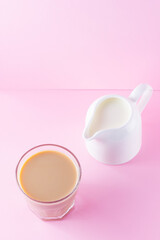 Milk tea on a pink background. Glass of masala chai tea and milk jug. Spiced tea and milk on a pastel background. Minimalism. Copy space