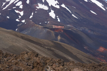 cratère de volcan rouge et brun foncé au pied d'un plus haut volcan au milieu d'un champ de lave 