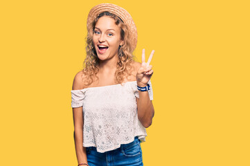 Beautiful caucasian woman wearing summer hat showing and pointing up with fingers number two while smiling confident and happy.