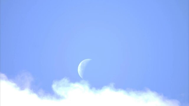 Time lapsed blue sky with white clouds rolling past a crescent moon