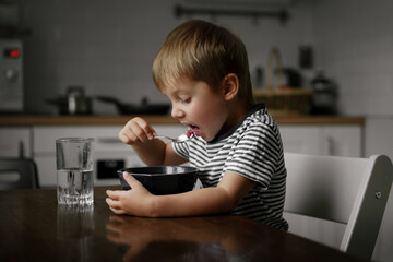 cute little boy looking at the bowl with porridge sitting at the table. Breakfast time. Image with selective focus